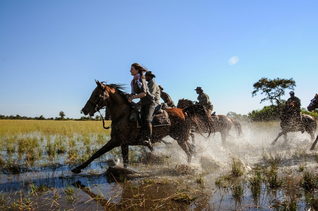 Women and guides galloping through water, African Horseback Safaris, Botswana