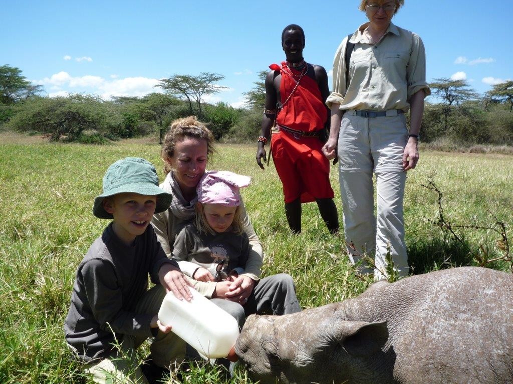 children and parent bottle feeding a baby rhino