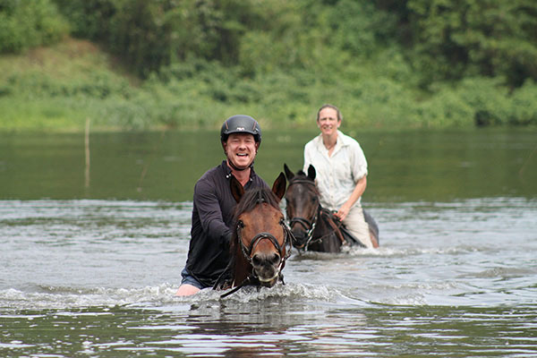 Riding safari in Uganda - horseriding couple swimming with their horses in the Nile