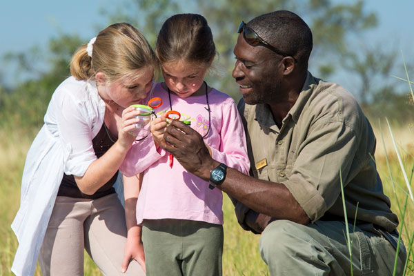 Two girls with magnifying glasses with safari guide, Seba Camp, Okavango Delta, Botswana